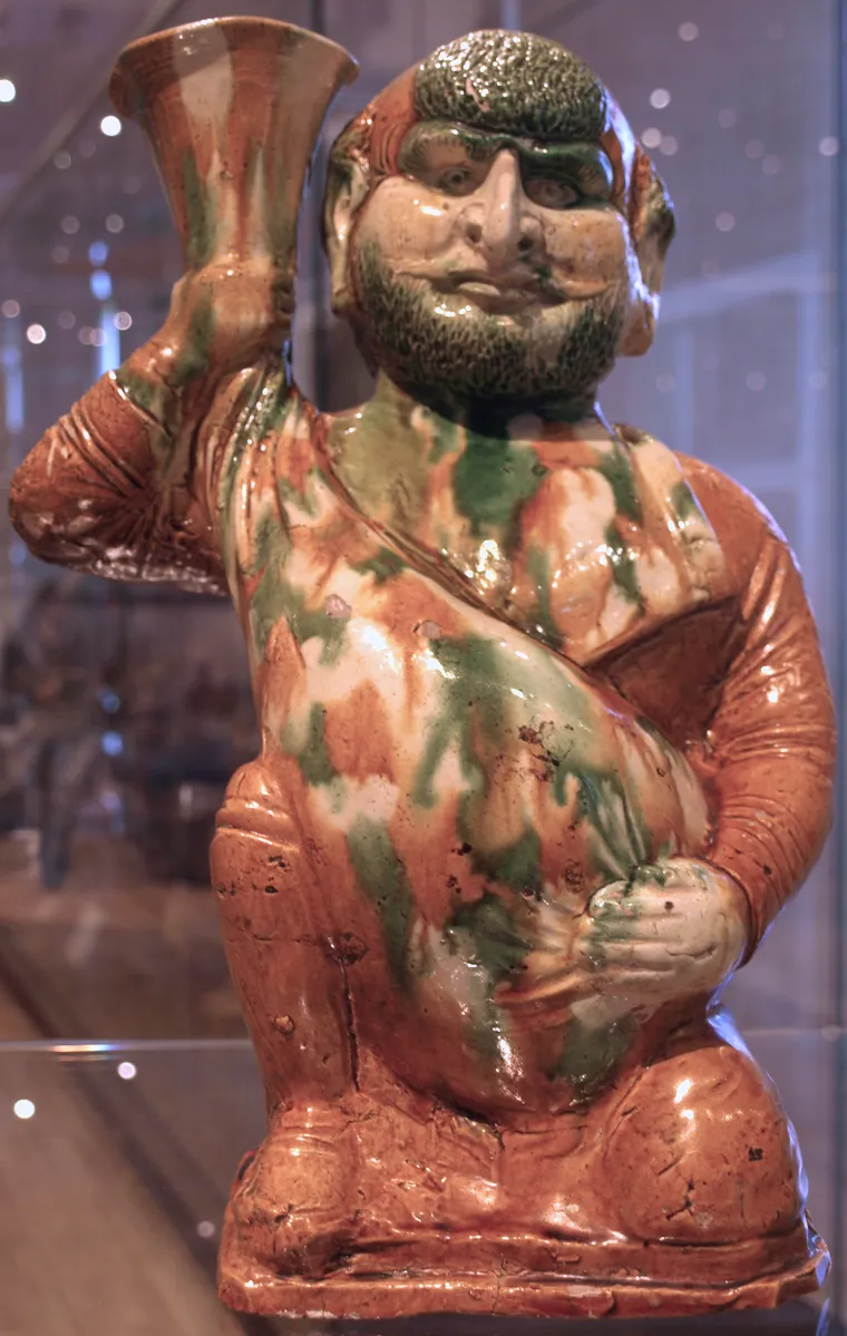Glazed earthenware figurine depicting a foreigner holding a wineskin. Circa 675-750 AD, Tang dynasty. Cat #918.21.7 The George Crofts Collection. From the Joey and Toby Tanenbaum Gallery of China at the Royal Ontario Museum. It most likely depicts an ethnic Sogdian considering the Sogdian wine merchant theme in Tang-era Chinese ceramic arts.